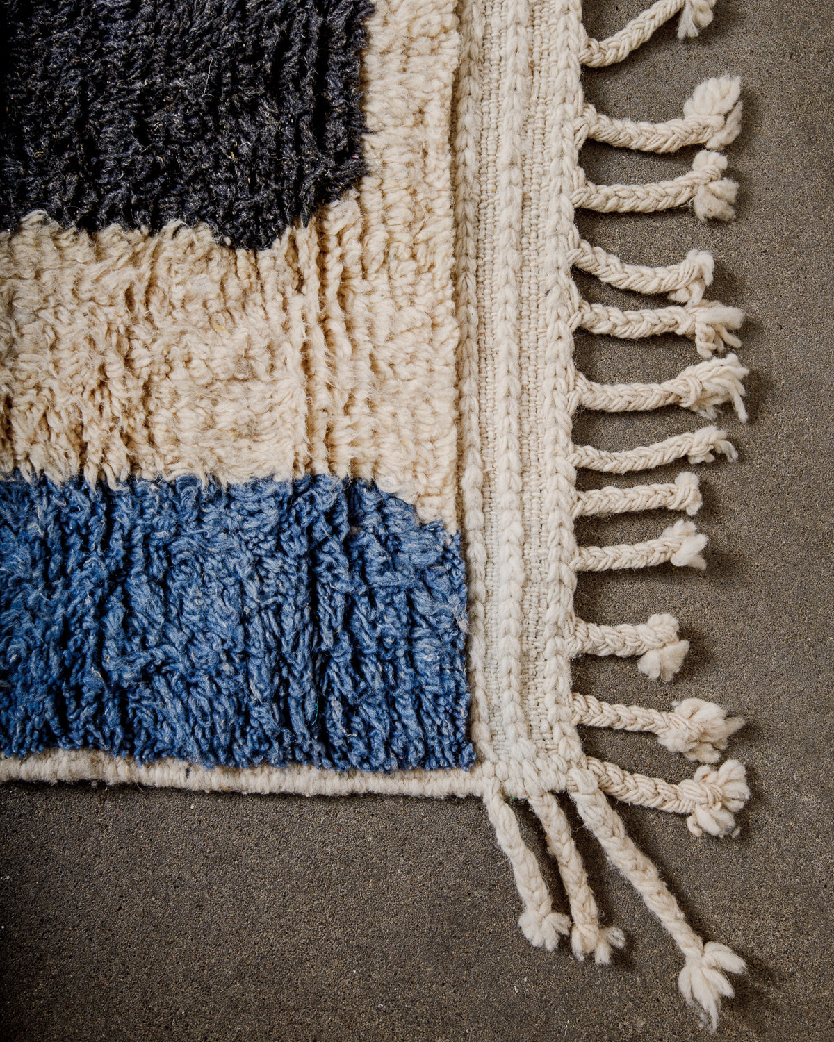 Corner of Berber runner rug with fluffy wool pile, tightly woven end and natural wool tassels.